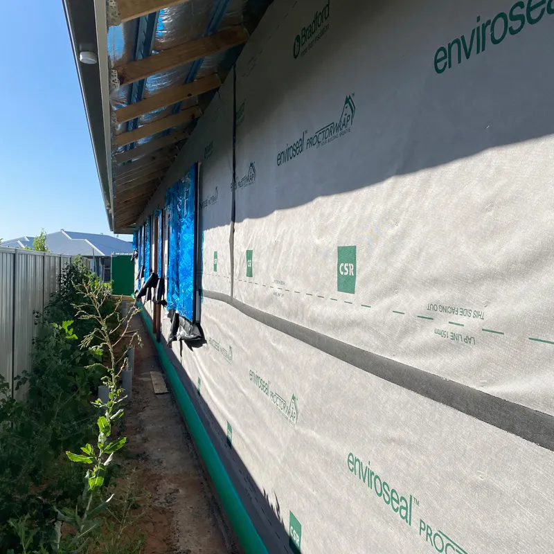 Wall wrap along the side of a new home beside a narrow garden bed